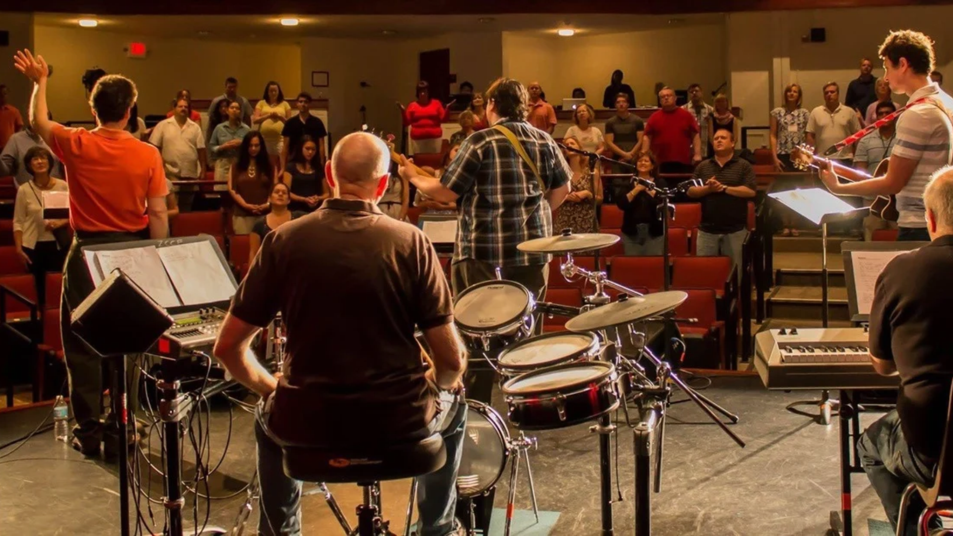 Small church worship team with drums, guitars, keyboard, and vocals leading a congregation during a worship service.
